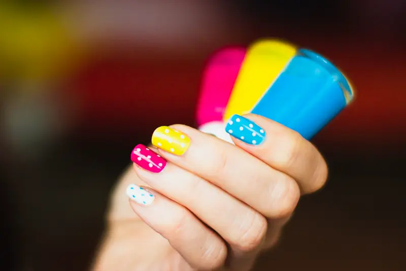 Bright multicoloured nails holding polish bottles