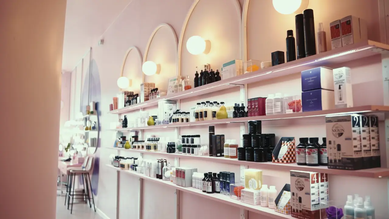 A bright beauty studio with blush-pink shelves of polishes and arched mirrors