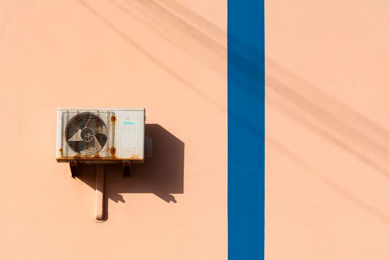 An aircon outdoor compressor on a bracket against a peach wall